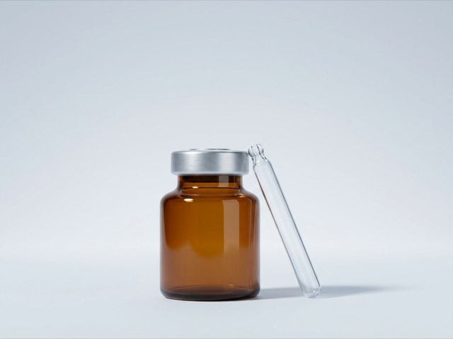 An amber glass vial beside a glass dropper pipette on a seamless pale grey ground