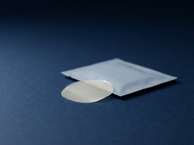 A thin translucent dissolving wafer and a plain sachet on a matte navy surface