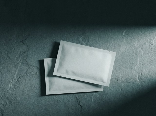Two plain sachets overlapping on a cool slate surface in low directional light