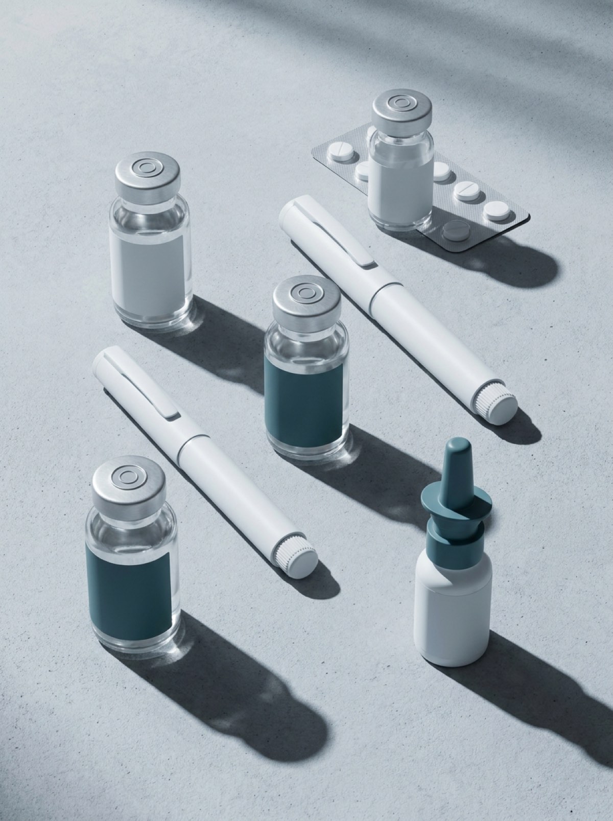 Unbranded vials, injector pens, a tablet blister and a nasal spray arranged on a pale grey surface under hard raking light
